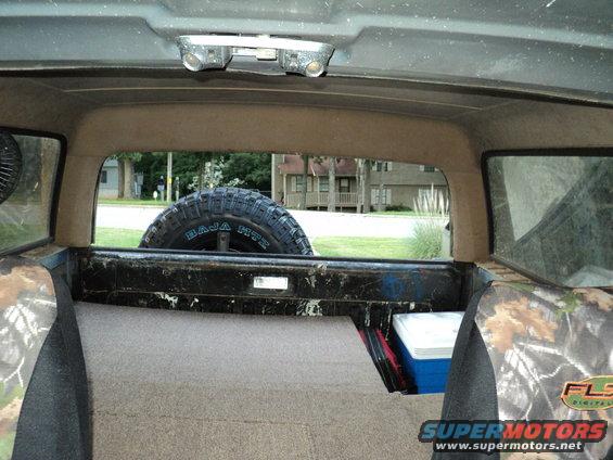 Interior view of an SUV showing camouflage seat covers, a cooler, and a spare tire mounted in the back