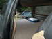 1986 Ford Bronco - The interior of a vehicle is shown with a bed, cooler, and fan, while a green SUV is visible outside.
