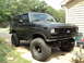 1986 Ford Bronco - This lifted Ford Bronco is parked in a driveway with trees in the background.