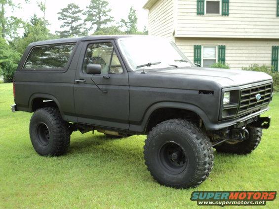 Black Ford Bronco with lifted suspension and large tires parked on grass in front of a house