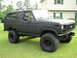 1986 Ford Bronco - This modified Ford Bronco sits on a grassy lawn, its off-road tires and dark matte paint job.