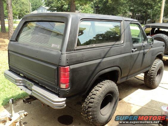 1986 Ford Bronco, rear 3/4 view, matte black with large off-road tires