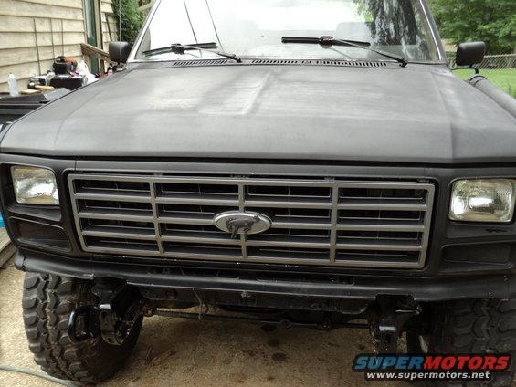 Front view of a matte black Ford Bronco with a chrome grille and a horse emblem. Lifted suspension and large tires are visible