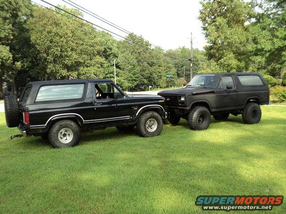 Two black Ford Broncos parked side-by-side on grass, one with a spare tire on the back