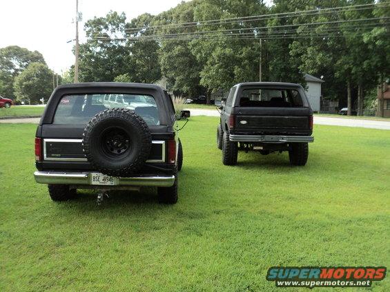 Rear view of two black 1986 Ford Broncos, one with a spare tire mounted on the back
