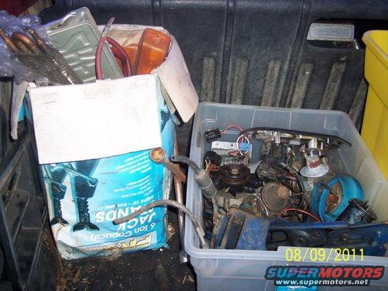 Plastic bin filled with engine parts and wiring; box contains car lights and other items
