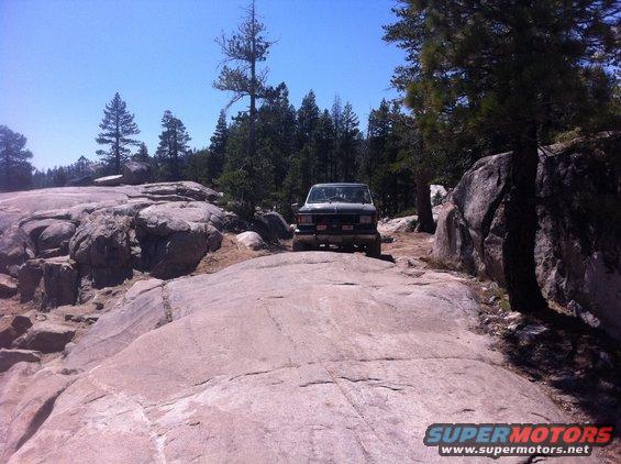 SUV driving on a rocky trail with trees and blue sky