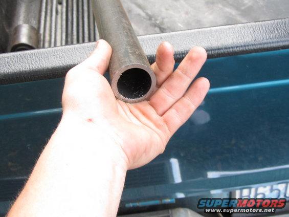 Hand holding a section of metal pipe over the bed of a teal pickup truck