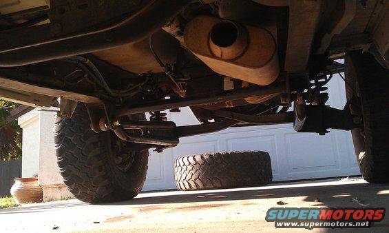 Underside view of a truck showing suspension, exhaust, and a spare tire on the ground