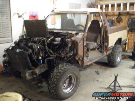 1987 Ford Bronco with hood open and engine removed, doors off, in a garage