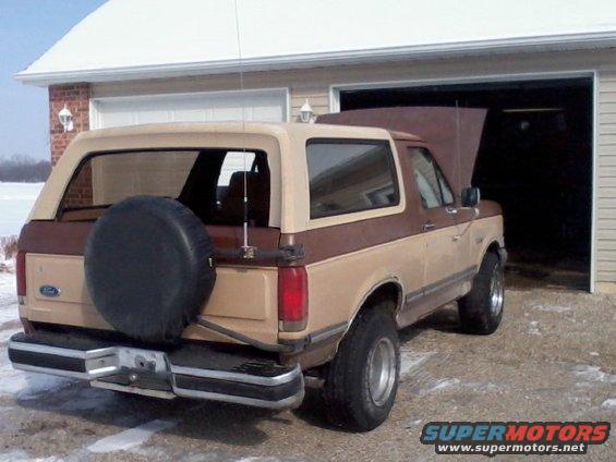 1987 Ford Bronco parked in front of a garage with hood open, spare tire on rear door