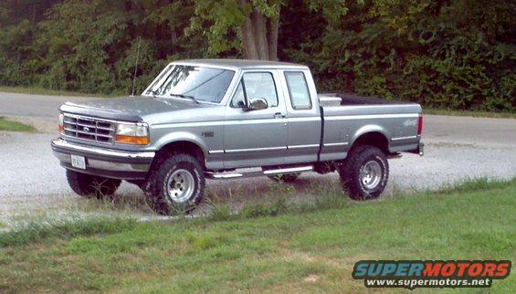 Silver 1995 Ford F-150 pickup truck with a crew cab and a toolbox in the bed, parked on a gravel surface