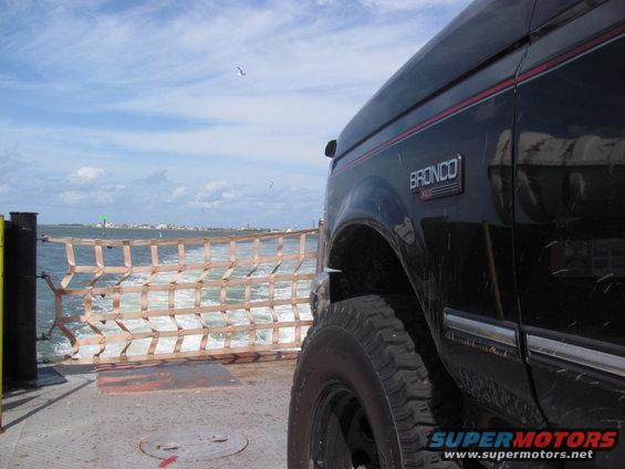 1995 Ford Bronco side view on a ferry crossing water, with a distant shoreline