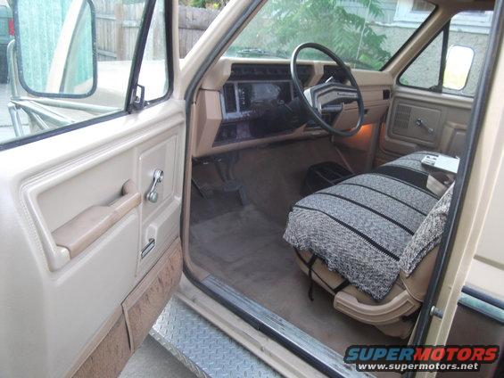 Interior view of a beige truck cab, showing the driver's seat with a blanket, dashboard, and steering wheel