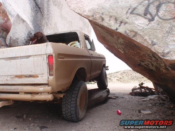 Brown 1977 Ford F-Series truck with a dog in the bed, parked under a rock overhang