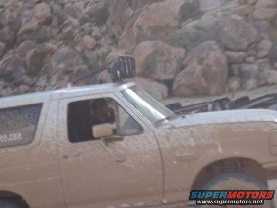 Mud-covered white Ford Bronco with a light bar on the roof, seen from the front-right