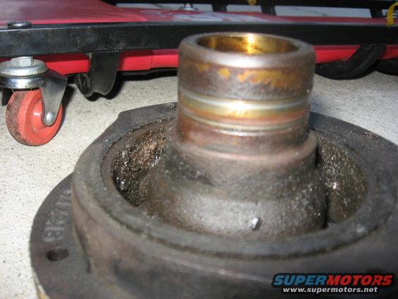 Used crankshaft pulley with worn bearing surface and debris, on a concrete floor near a red creeper
