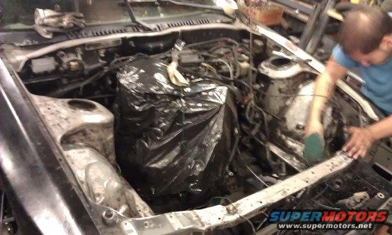 Engine bay with engine covered in plastic, being cleaned