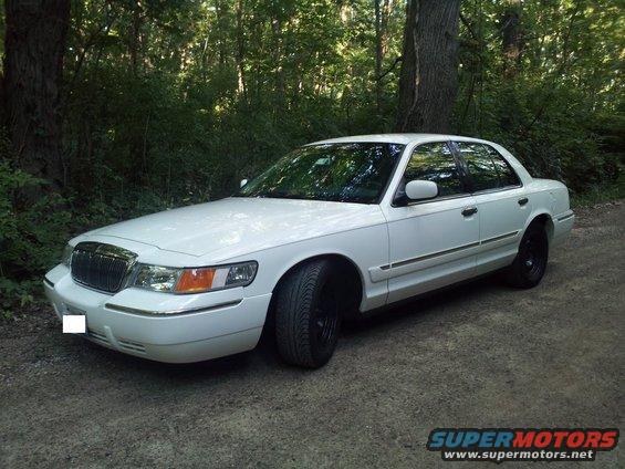 White 2000 Mercury Grand Marquis parked on a dirt road with trees in the background