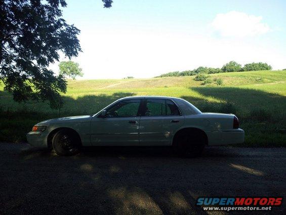 Light-colored sedan parked on a dirt road, side view, with tinted windows and black wheels