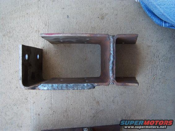 Welded steel bracket with two mounting holes on the left flange, resting on concrete