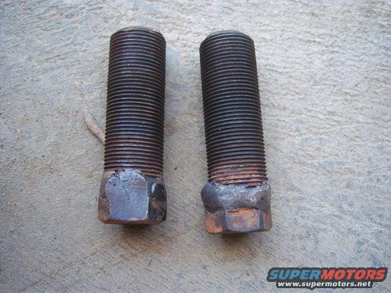 Two rusty threaded bolts with hex heads, lying on a concrete surface