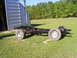 1992 Ford Bronco - The bare chassis of a vehicle sits on a grassy field next to a large metal structure.