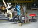 1992 Ford Bronco - Front axle and suspension components are visible, with a bright blue coil spring and a yellow strap supporting the assembly.