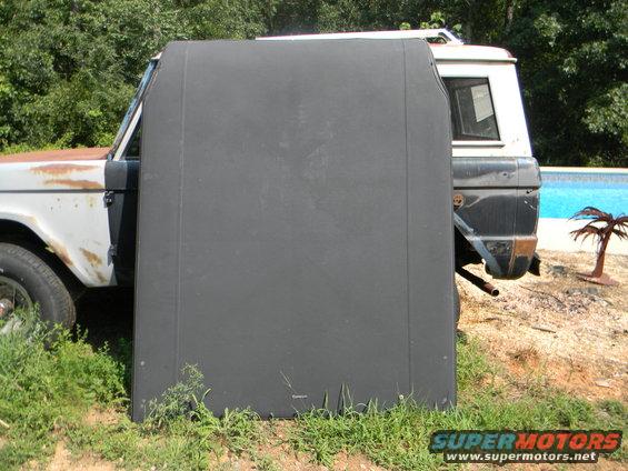 Side view of a white and rusty Ford Bronco with a black soft top in front of it. Another Bronco is partially visible behind it