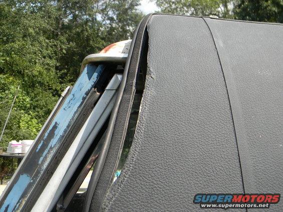 Close-up of a dark gray vinyl roof edge and peeling blue paint on a vehicle window frame