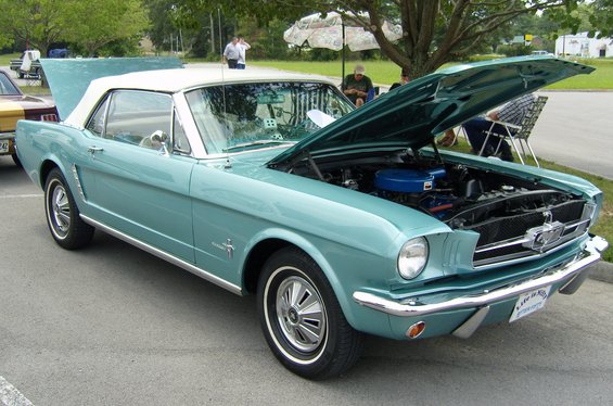 Teal 1965 Ford Mustang convertible with white top, hood open, showing engine. Chrome trim, whitewall tires