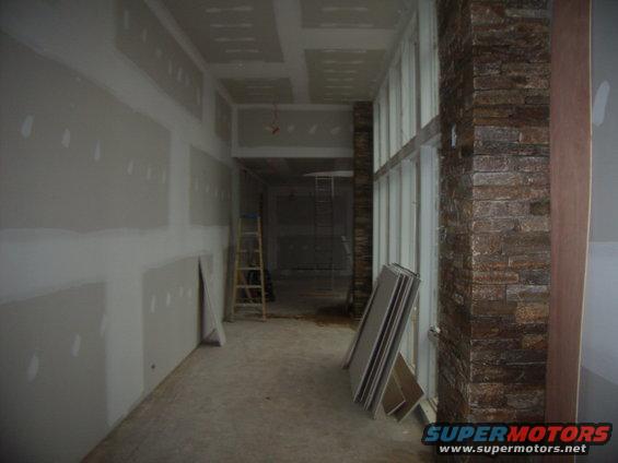 Interior hallway under construction with drywall, a ladder, and stacked drywall sheets