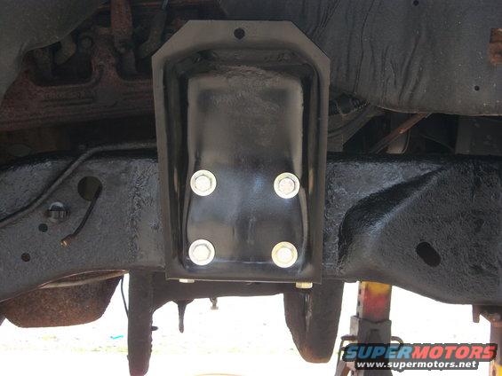 Black metal bracket bolted to vehicle frame, showing four silver bolts