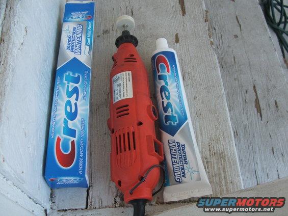Orange rotary tool with a white polishing wheel, next to a box and tube of Crest toothpaste