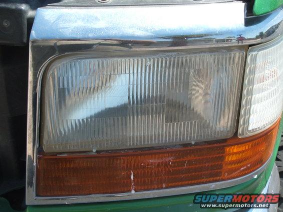 Close-up of a 1992 Ford Bronco headlight assembly with chrome trim and amber turn signal