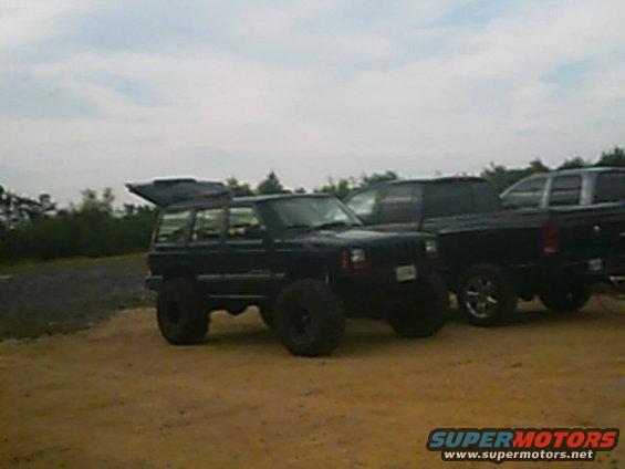 Black Jeep Cherokee XJ with lifted suspension and large tires parked next to a black pickup truck