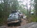1988 Ford Bronco - Multiple off-road vehicles navigate a challenging path through a dense forest.