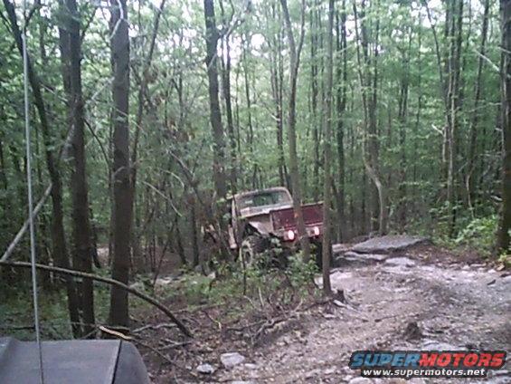 Red off-road truck with a lifted suspension navigating a rocky, wooded trail