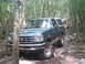 1988 Ford Bronco - A green Ford Bronco navigates a challenging rocky path through a wooded area, with another vehicle visible further down the trail.
