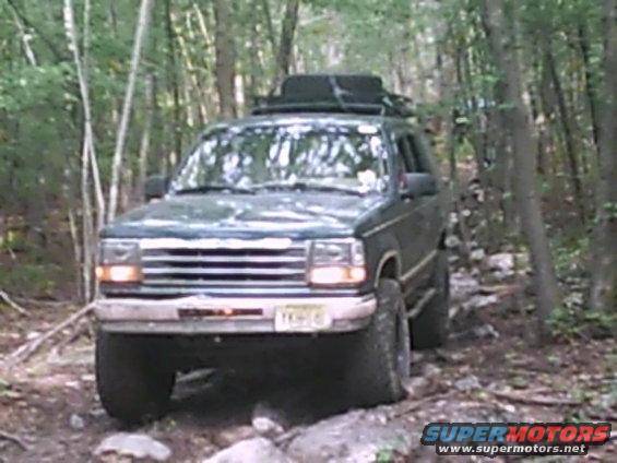 Dark green Ford Explorer on a rocky, wooded trail with a roof rack