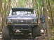 1988 Ford Bronco - A dark-colored Ford Bronco navigates a wooded trail, its large tires gripping the terrain.