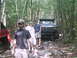 1988 Ford Bronco - A dark blue Ford truck navigates a rocky path through a wooded area with several people nearby.
