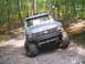 1988 Ford Bronco - Gray Ford Bronco with large tires navigates a wooded trail during an off-road event.