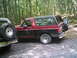 1988 Ford Bronco - A red and black 1988 Ford Bronco is parked in a wooded area next to another vehicle.