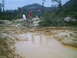 1988 Ford Bronco - Off-road terrain with puddles and people walking. The scene is hilly and wooded.