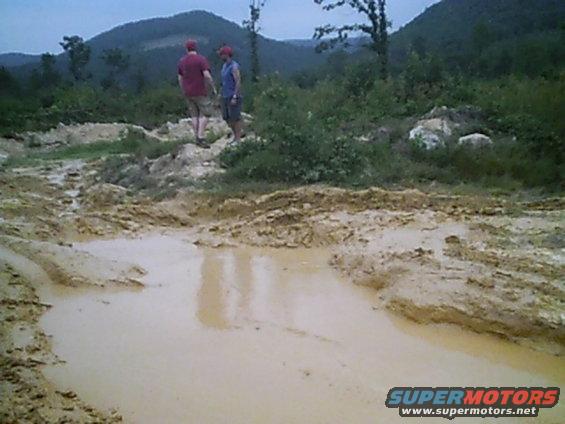 two people standing near a muddy puddle on an off-road trail