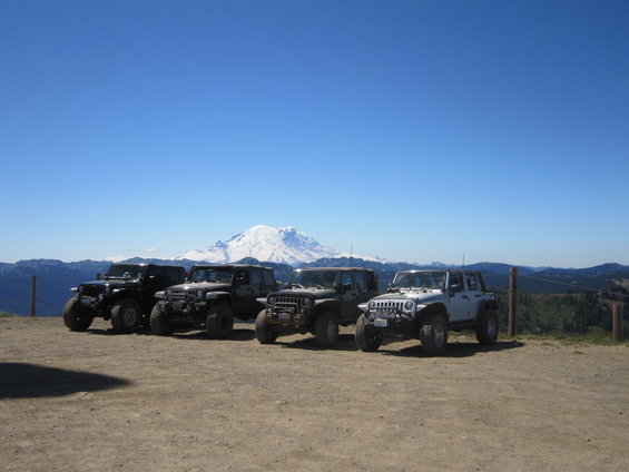 Four Jeeps parked on a dirt overlook with a snow-capped mountain in the background