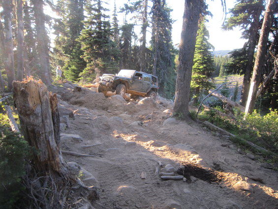 Jeep Wrangler climbing a steep, rocky, dirt trail through a forest