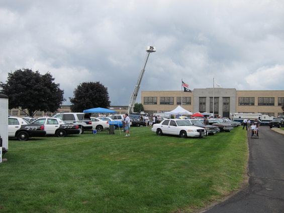 Several police cars and other vehicles parked on grass in front of a building with a fire truck ladder extended