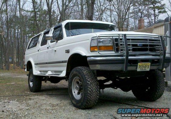 White extended SUV with off-road tires and a brush guard, seen from the front-right